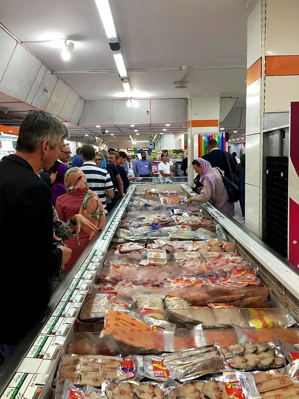 Visitors browsing a supermarket seafood freezer aisle