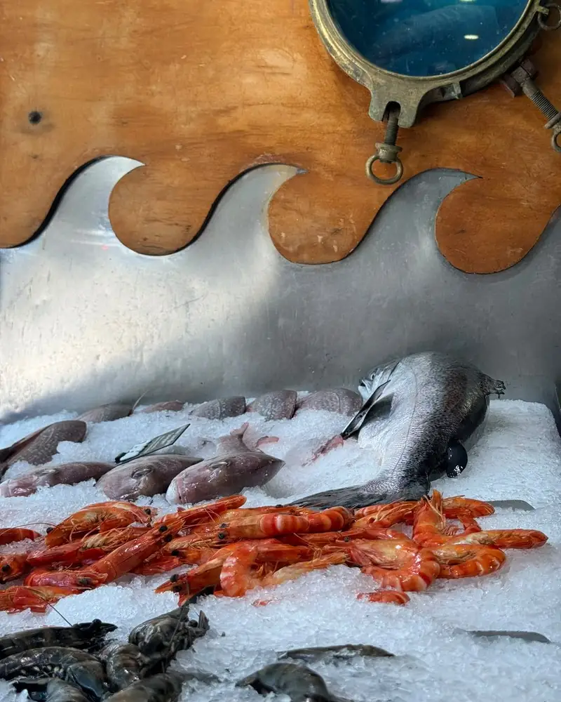 Cooked prawns, raw tiger prawns and whole fish on ice at a seafood counter